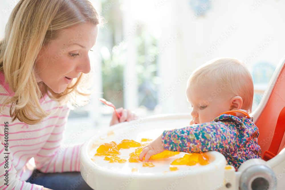 Mother feeding baby girl in high chair Mother feeding baby girl in high chair