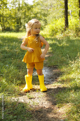 a beautiful blonde girl in a linen suit is standing in the park and catching raindrops there are yellow boots nearby