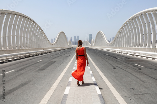 Photography One woman in an orange red dress walking by an empty road on a Meydan bridge wit