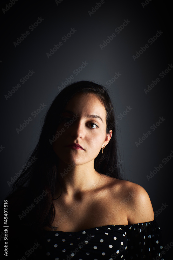 Close-up portrait of a young girl with a serious look looking towards the camera, on a dark studio background