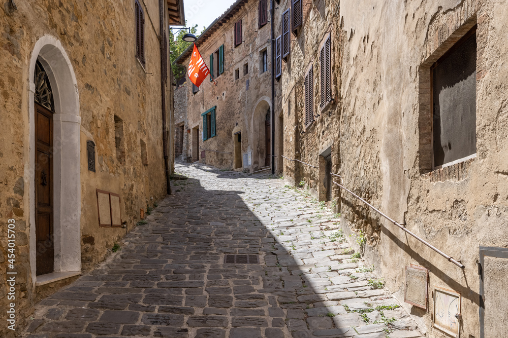 A narrow medieval stone paved street with a red waving flag in the tuscanian town of Montalcino