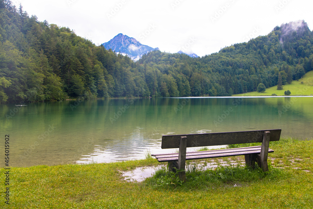 Beautiful panoramic landscape with a mountain lake and a wooden bench. The lake called Alatsee in German. Near Füssen, Allgäu, Germany