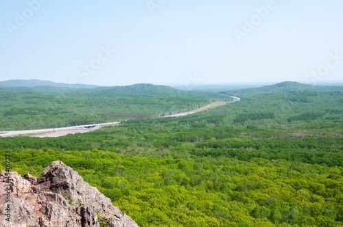 Summer landscape, part of a cliff and a green forest, a road in the distance