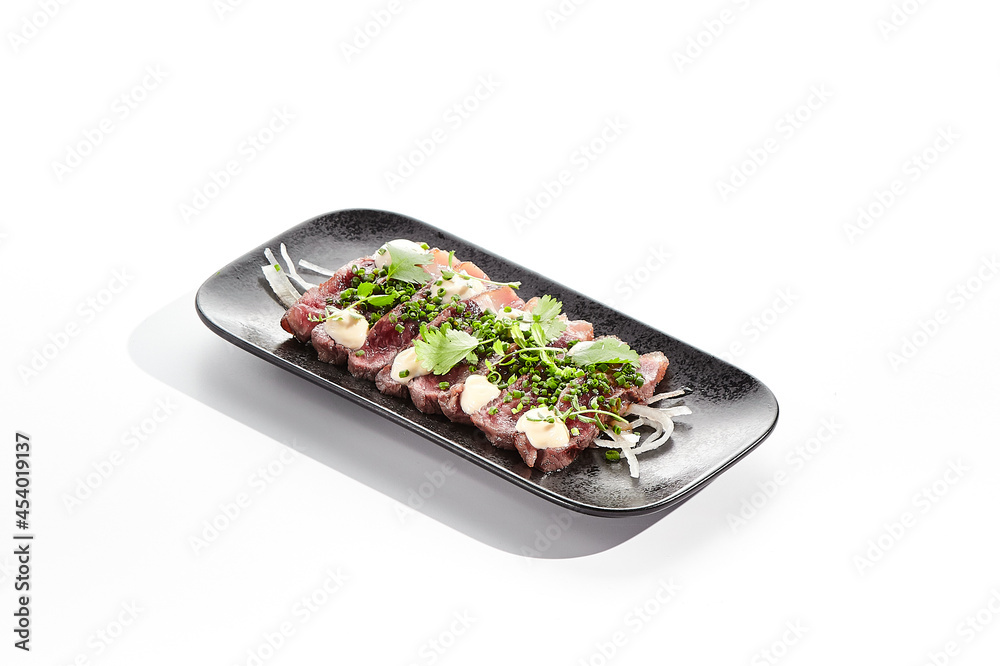 Beef tataki - seared beef,. thinly sliced sashimi style. Beef tataki served with delicious ponzu tataki sauce. Japanese style meat on black plate isolated on white background..
