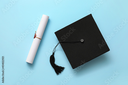 Фотография Graduation hat and diploma on color background