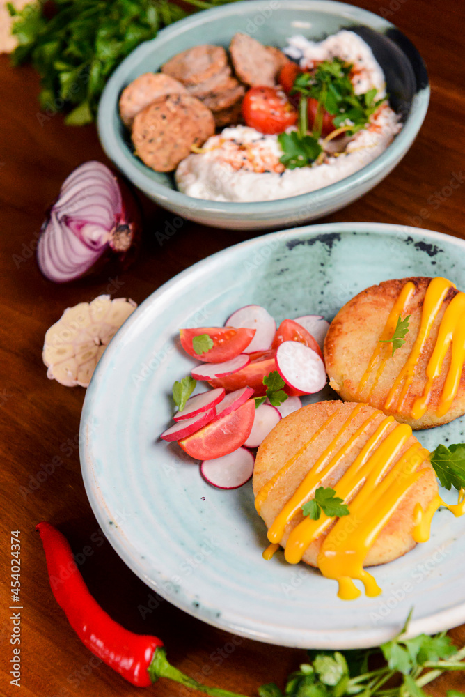 Grilled burgers with sauce and vegetable radish salad on a plate on a rustic wooden table background. Grilled burgers with sauce and vegetable radish salad on a plate on a rustic wooden table background.