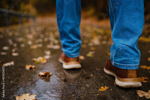 feet of a woman walking along asphalt road in autumn forest