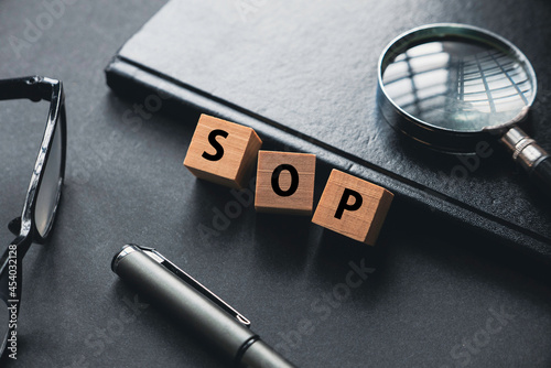 Selective focus of glasses, magnifying glass, notebook, pen and wooden cube written with SOP or Standard Operating Procedure.