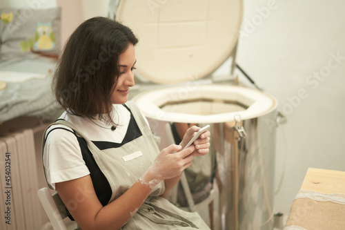 Female potter using smartphone in workshop