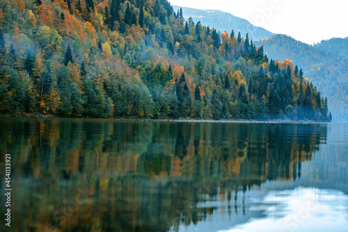 Beautiful view on the mountain lake with the colorful autumn trees on the hills.