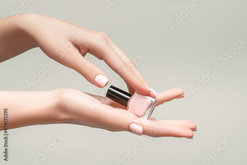 Female hands with pink nail design. Pink fingernails manicure. Woman hands hold pink nail polish on beige background