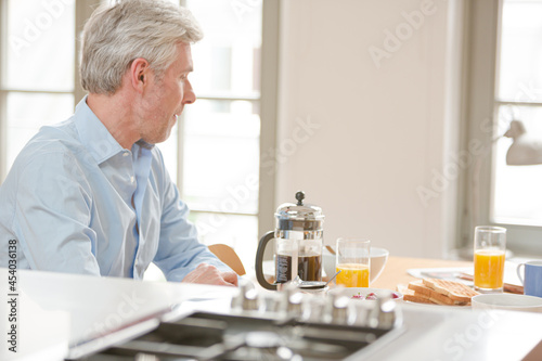 Older man reading newspaper at breakfast table