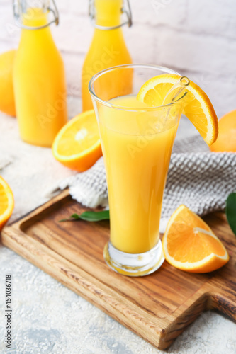 Board with glass of tasty orange juice on light background