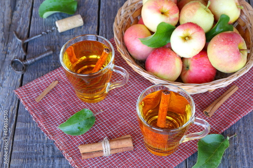 Apple cider in glass mugs near wicker basket with fresh fruit on the old wooden table. 