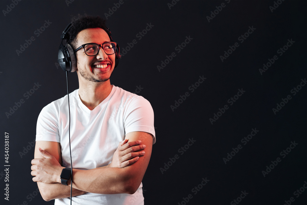 Young African American man wearing headphone, white t shirt and enjoy music over black Background. Red light reflecting on face. Emotions and face expressions Young African American man wearing headphone, white t shirt and enjoy music over black Background. Red light reflecting on face. Emotions and face expressions