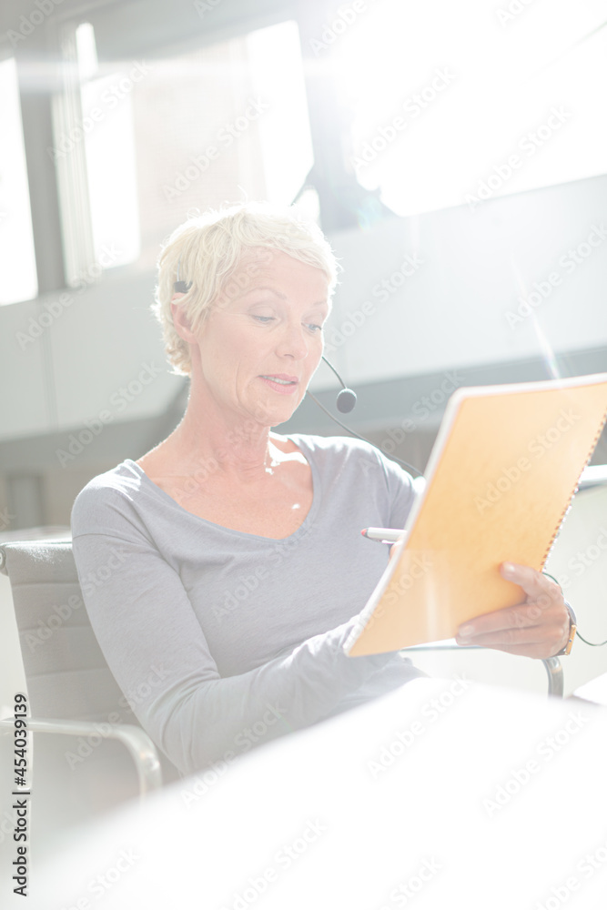 Businesswoman in headset writing on notepad in office Businesswoman in headset writing on notepad in office