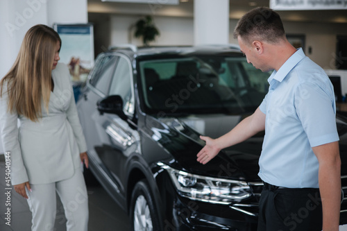 Salesperson shop opporrtunity of each car and help her choos and make right decision. Man and woman in car showroom