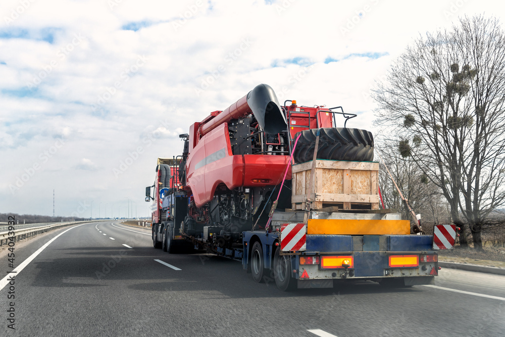 Φωτογραφία Heavy industrial truck with semi trailer platform transport disassembled combine harvester machine on common public highway road on sunset sunrise day