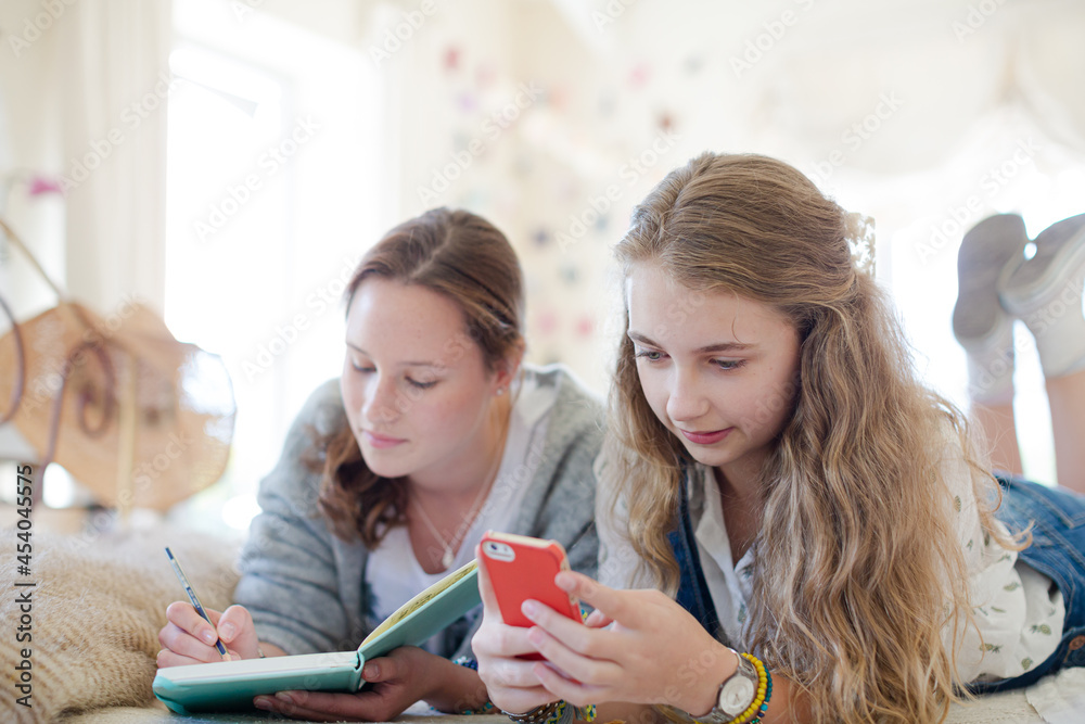 Two teenage girls on bed writing in notepads Two teenage girls on bed writing in notepads