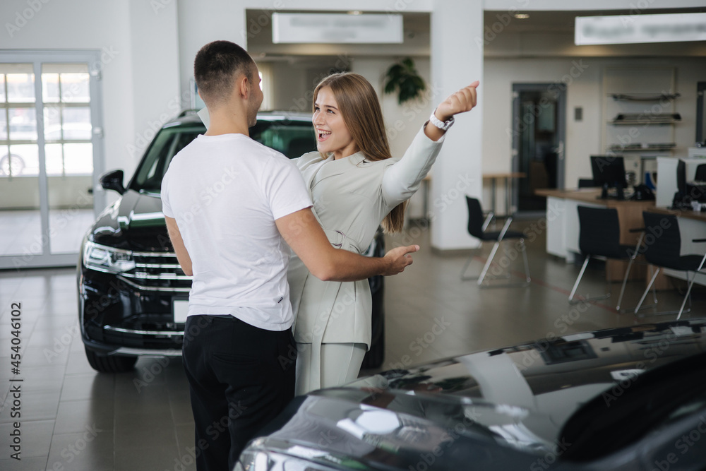 Happy woman hug his husband afrer buying car in car showroom. Man and woman buy new car