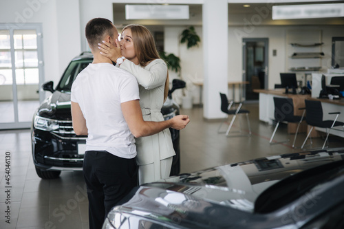 Happy woman hug his husband afrer buying car in car showroom. Man and woman buy new car © Aleksandr