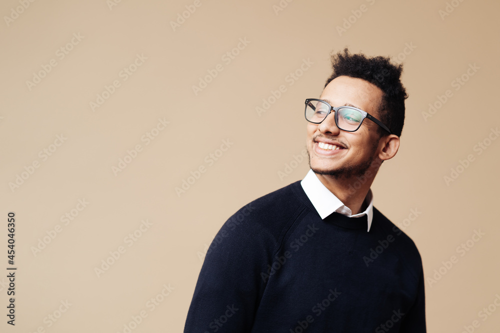 Young handsome man wearing sweater, white shirt and glasses looking at copy space on beige background face smiling looking at the camera. Positive person, professor style Young handsome man wearing sweater, white shirt and glasses looking at copy space on beige background face smiling looking at the camera. Positive person, professor style