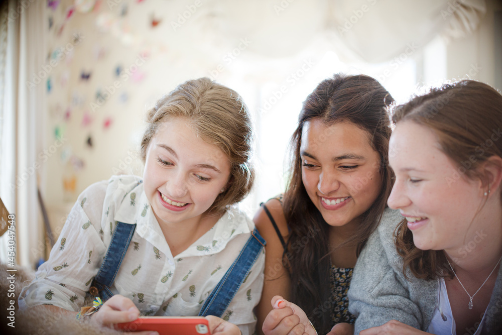 Three teenage girls using smart phone together while lying on bed Three teenage girls using smart phone together while lying on bed