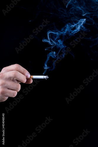 Black background. the hand of a man with roughened skin holds a cigarette. blue smoke is coming from it. close-up.