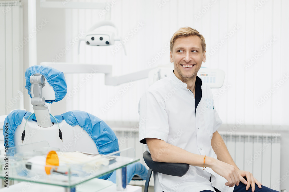 Obraz premium Portrait of a positive young male dentist in uniform at the dental office
