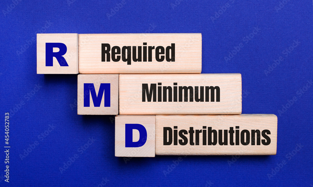 On a bright blue background, light wooden blocks and cubes with the text RMD Required Minimum Distributions