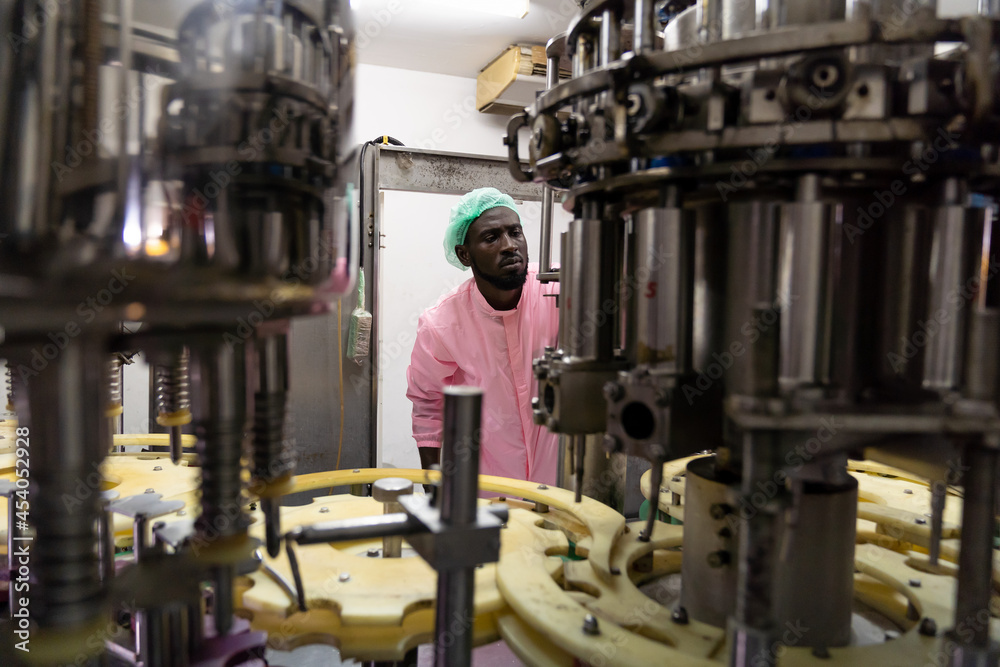 Controller worker working checking automated conveyor belt at beverage factory. African American male engineer worker working or maintenance with the machine in the industrial factory Controller worker working checking automated conveyor belt at beverage factory. African American male engineer worker working or maintenance with the machine in the industrial factory