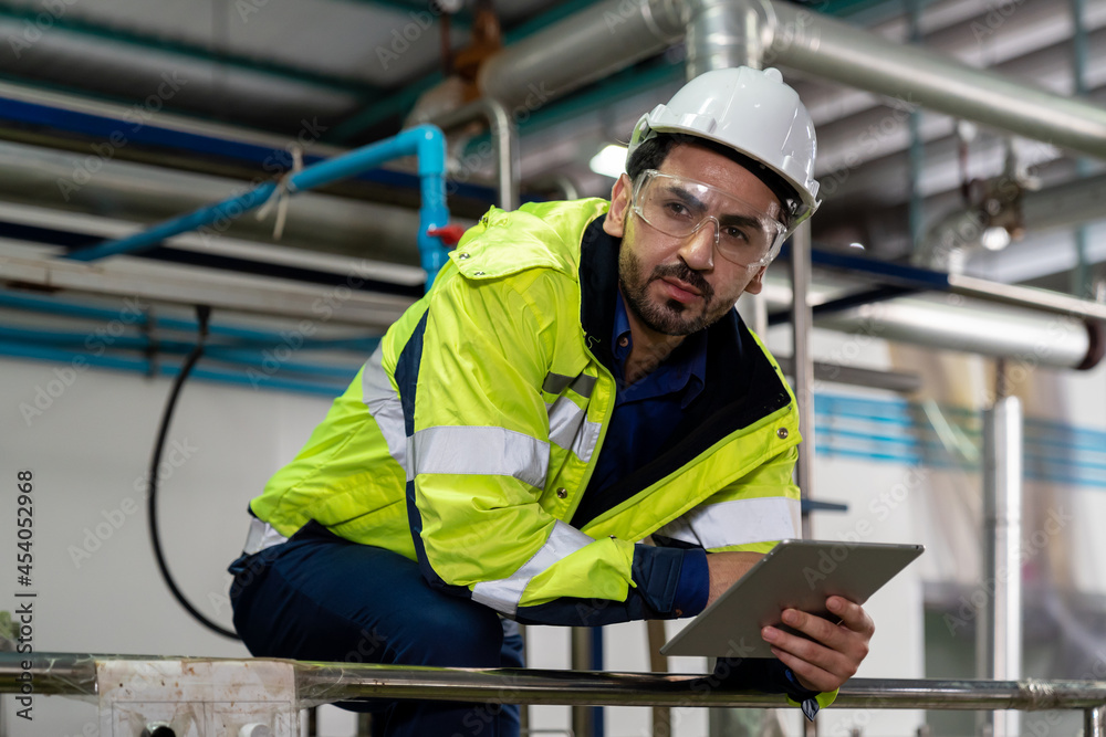Male factory mechanic wearing safety glasses, white helmet. Technicians male working with digital tablet, checking the operation of equipment, repairing and maintenance machinery in industry factory Male factory mechanic wearing safety glasses, white helmet. Technicians male working with digital tablet, checking the operation of equipment, repairing and maintenance machinery in industry factory