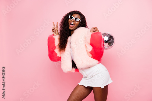 Photo of attractive brunette dark skin nice lady make v-sign hold disco ball isolated on pastel pink color background