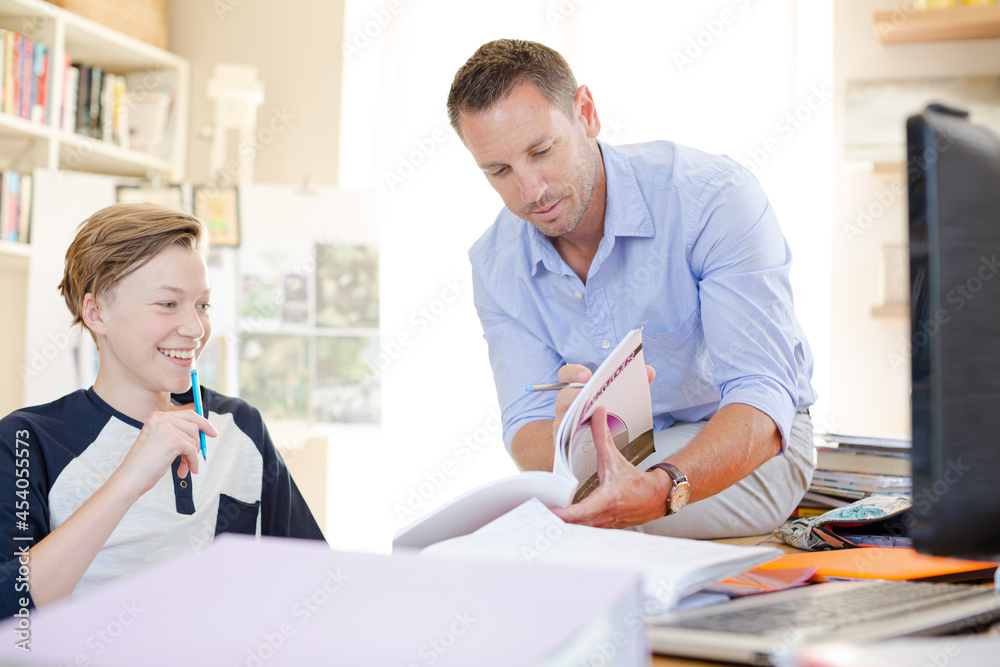 Father helping teenage son doing his homework in room
