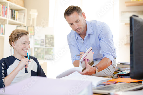 Father helping teenage son doing his homework in room