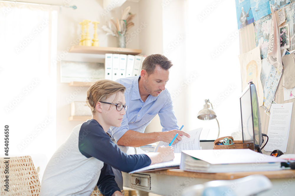 Father helping teenage son doing his homework in room