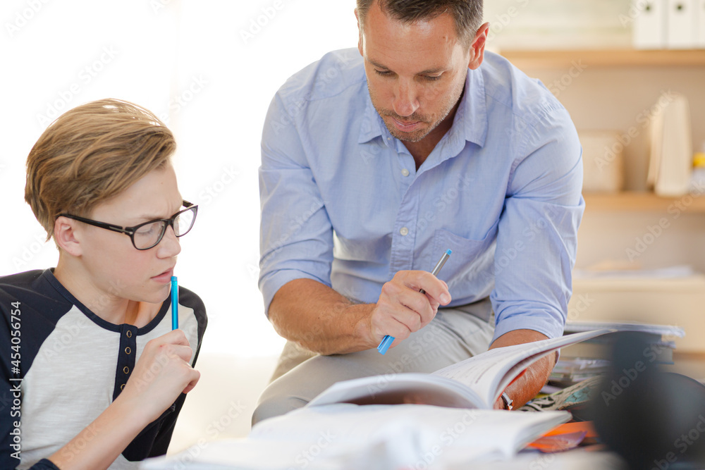 Fototapeta premium Father helping teenage son doing his homework in room