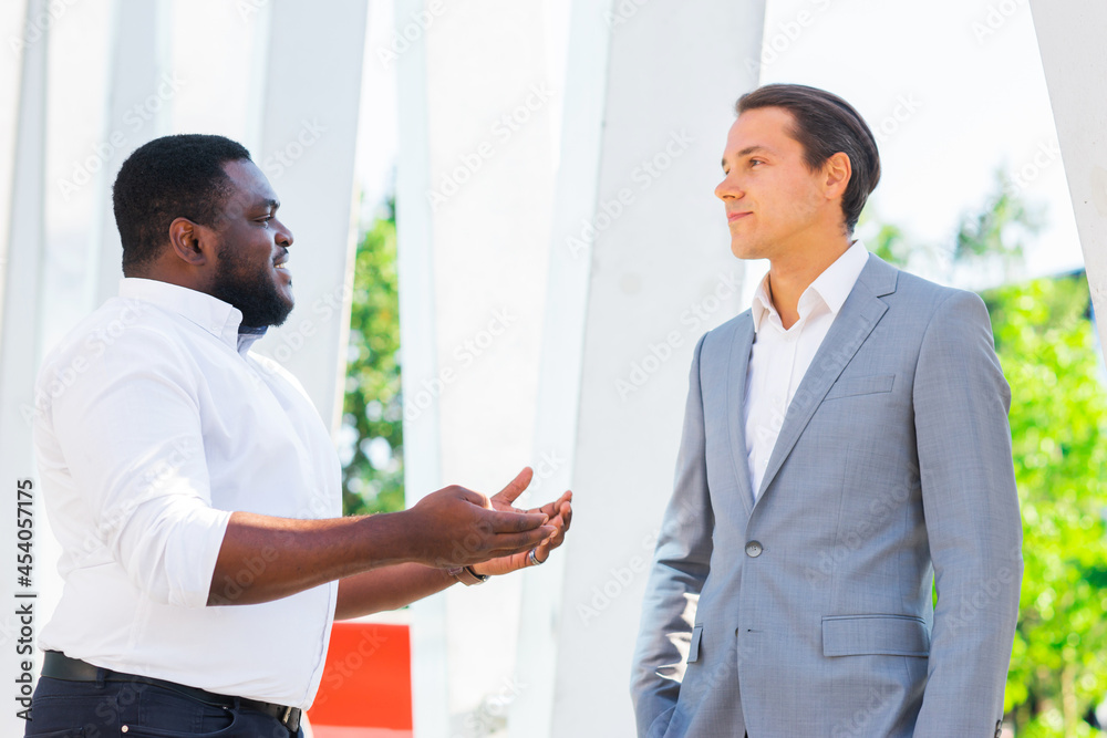 African-American businessman and his colleague in front of modern office building. Financial investors are talking outdoor. Banking and business concept.
