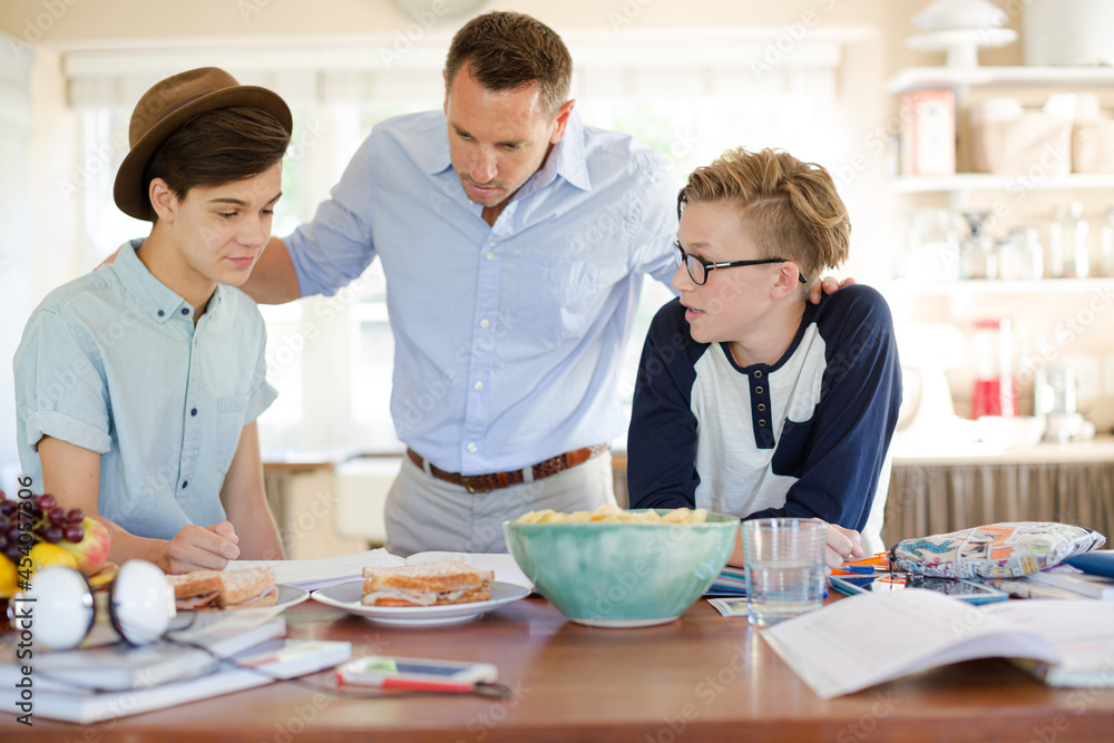 Teenage boys with father using laptop in dining room Teenage boys with father using laptop in dining room