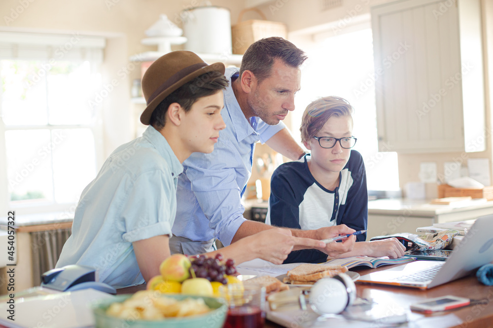 Teenage boys with father using laptop in dining room