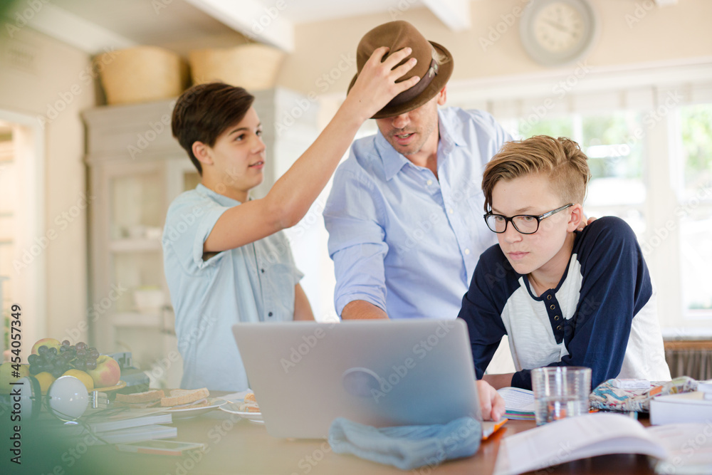 Teenage boys with father using laptop in dining room Teenage boys with father using laptop in dining room