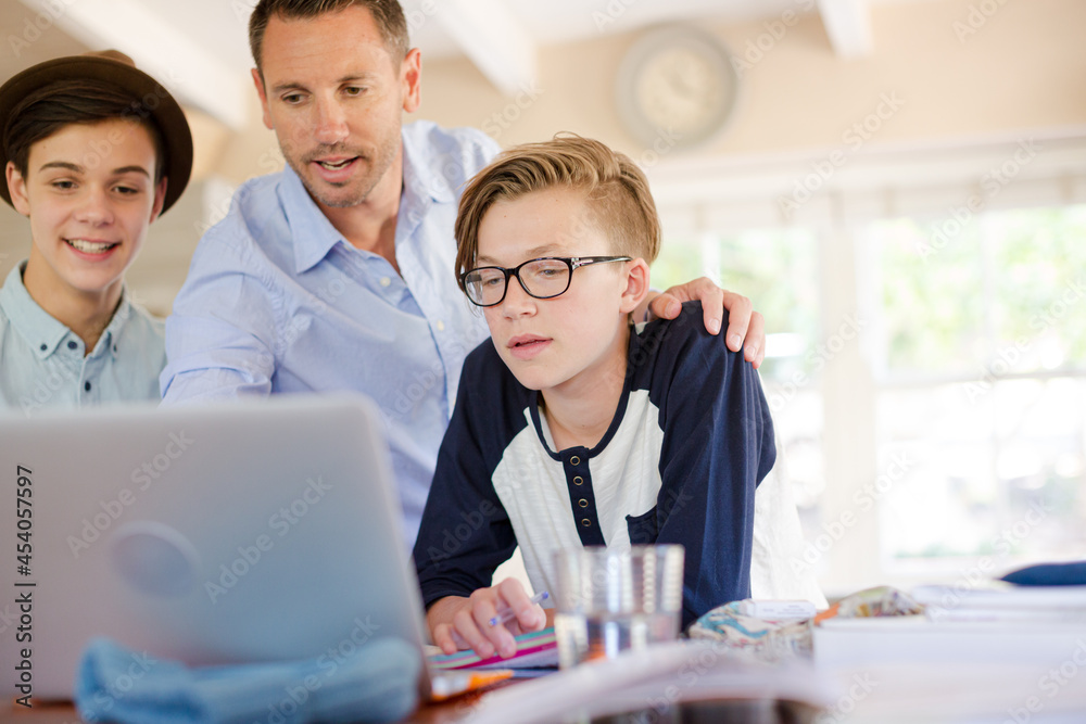 Teenage boys with father using laptop in dining room Teenage boys with father using laptop in dining room