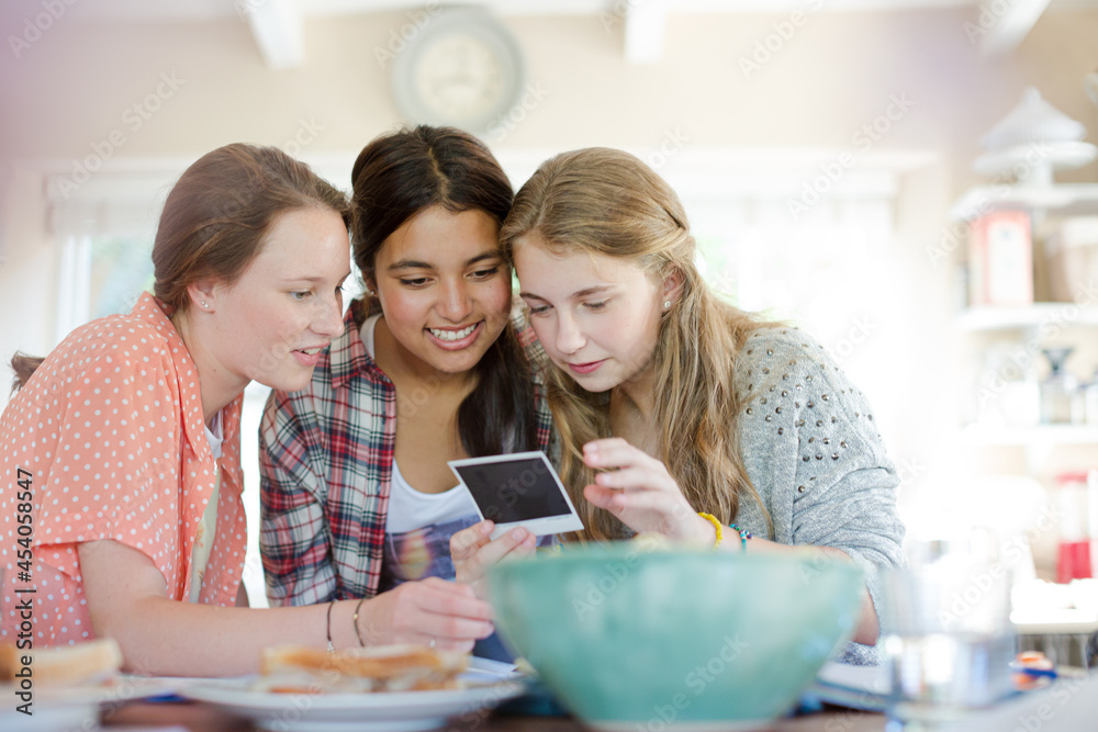 Three teenage girls looking at photograph while sitting at table Three teenage girls looking at photograph while sitting at table