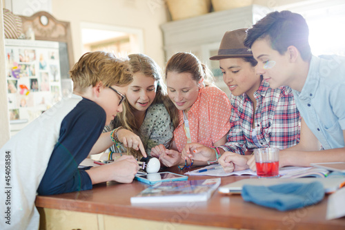 Group of teenagers using together digital tablet at table in kitchen