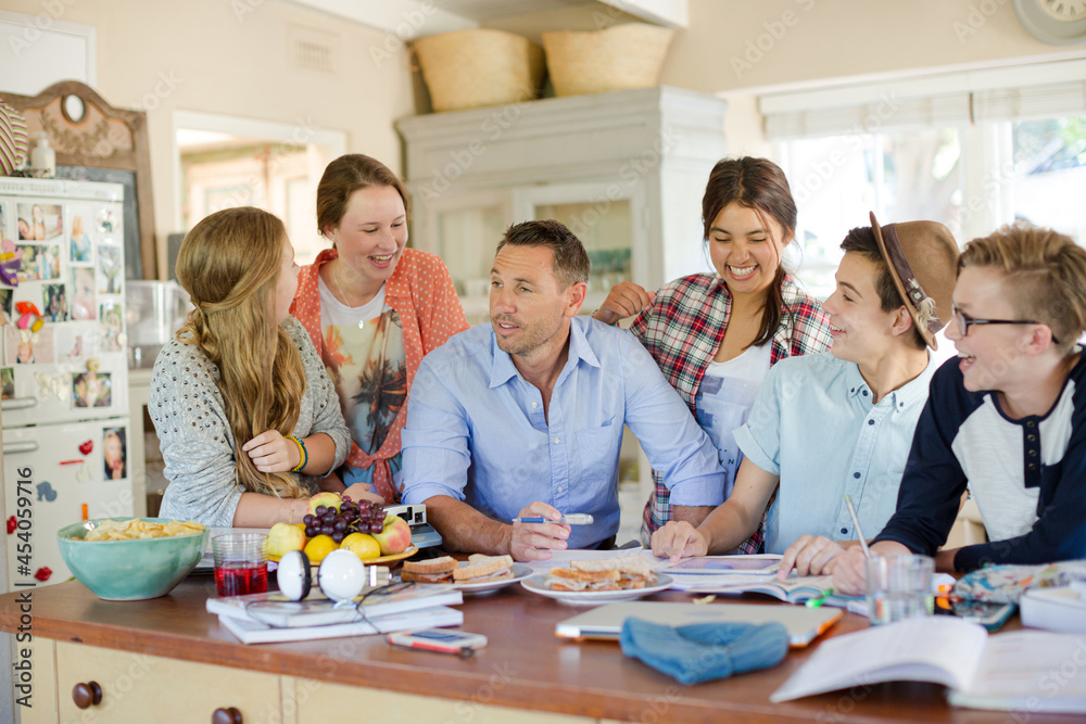 Fototapeta premium Teenagers with mid adult man sitting at table in dining room