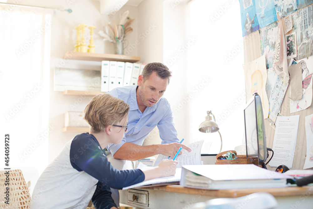Father helping teenage son doing his homework in room Father helping teenage son doing his homework in room