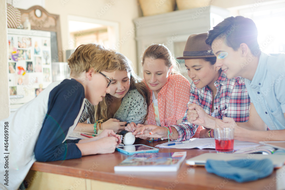 Group of teenagers using together digital tablet at table in kitchen Group of teenagers using together digital tablet at table in kitchen