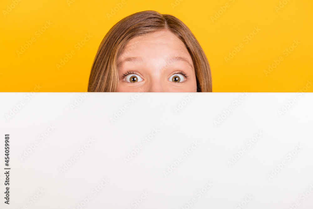 Photo of little girl eyes peeking behind large empty space wall look camera isolated on yellow color background Photo of little girl eyes peeking behind large empty space wall look camera isolated on yellow color background