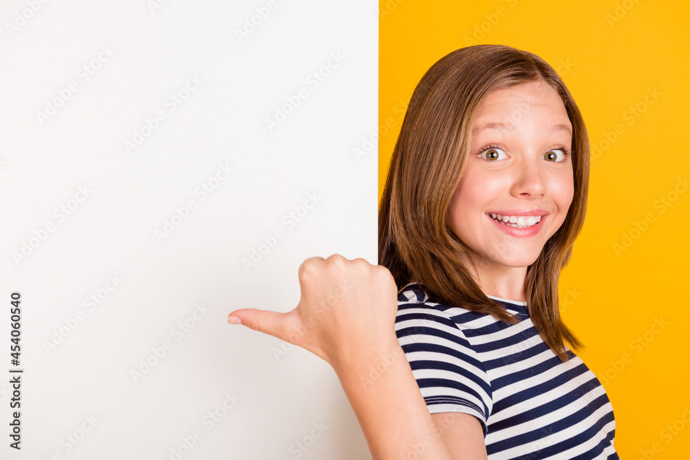 Photo of positive pupil indicate thumb empty space promotion toothy smile isolated on yellow color background Photo of positive pupil indicate thumb empty space promotion toothy smile isolated on yellow color background