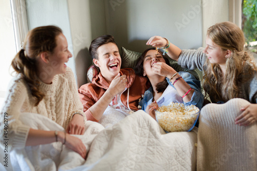 Group of teenagers throwing popcorn on themselves on sofa